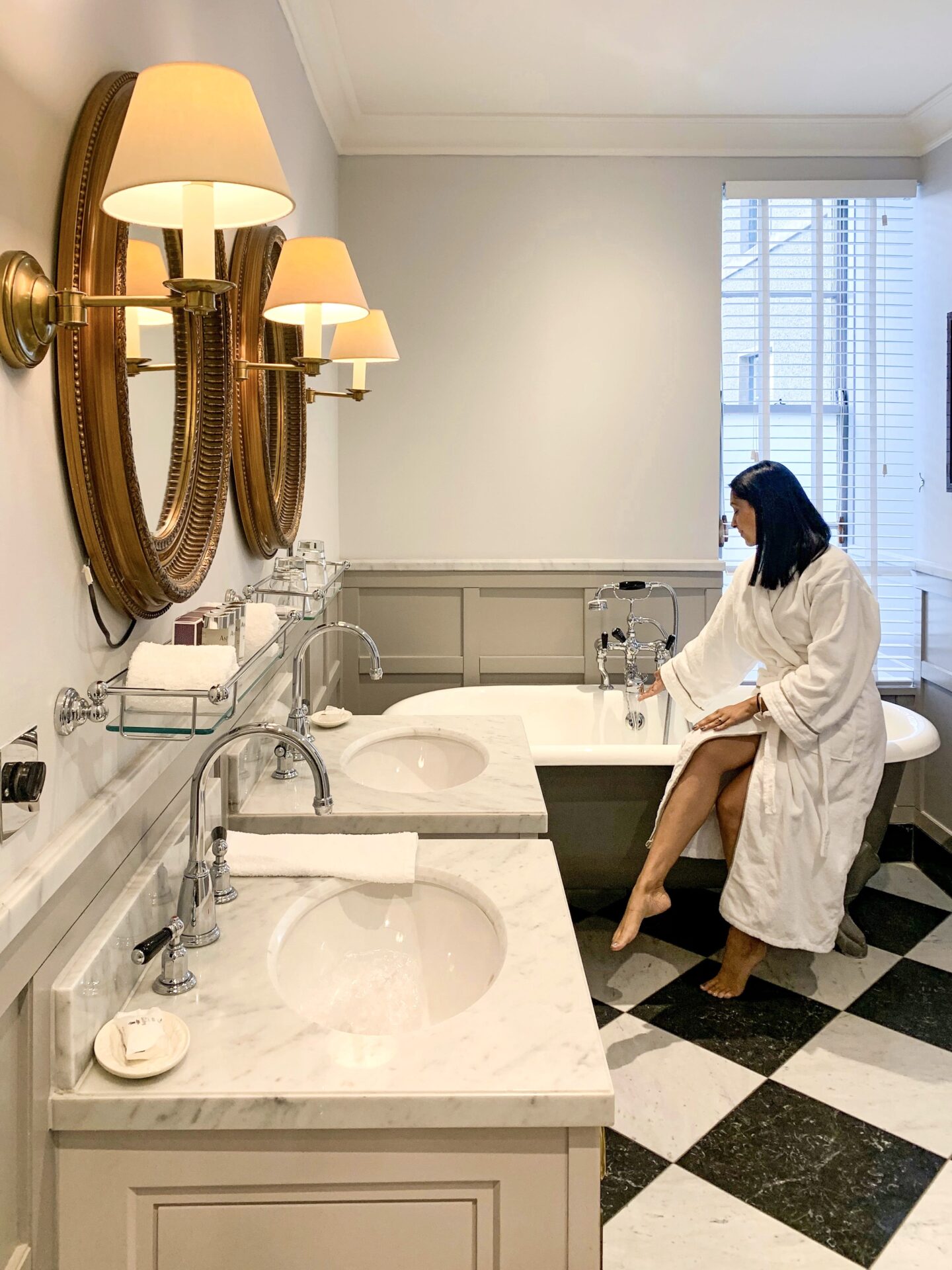 sima sat on the side of the bath in the gleneagles luxury hotel with and black floor tiles and marble worktops around sinks
