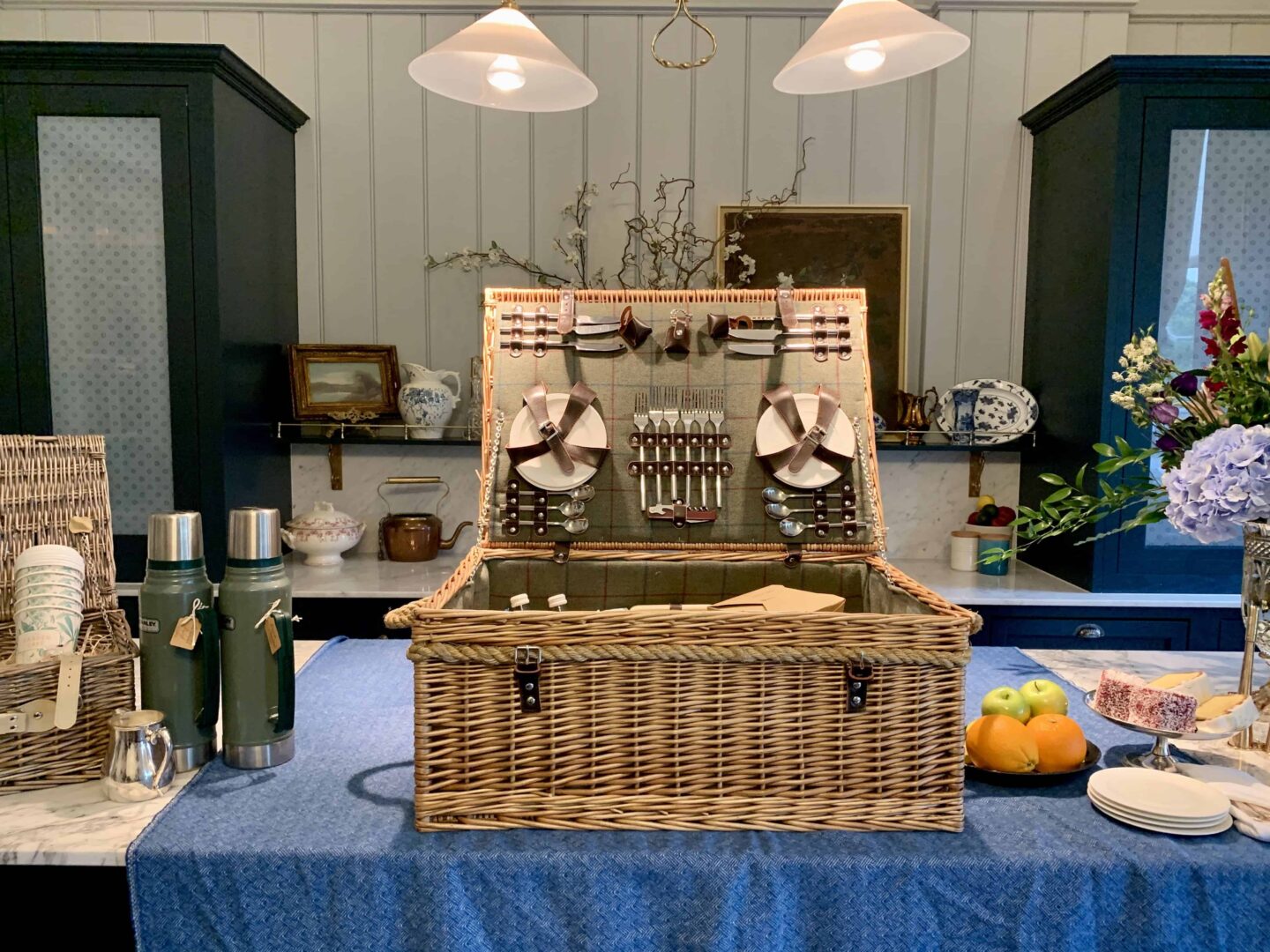view of a wicker picnic basket with all accessories on a blue table cloth