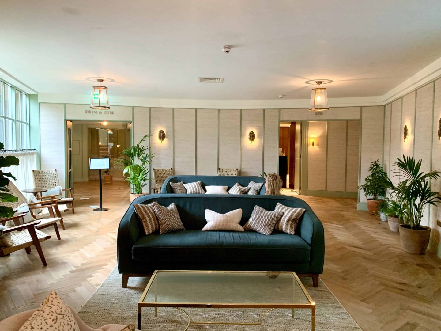 view of the spa waiting area with blue sofas and sand coloured cushions on a wooden floor and green foliage