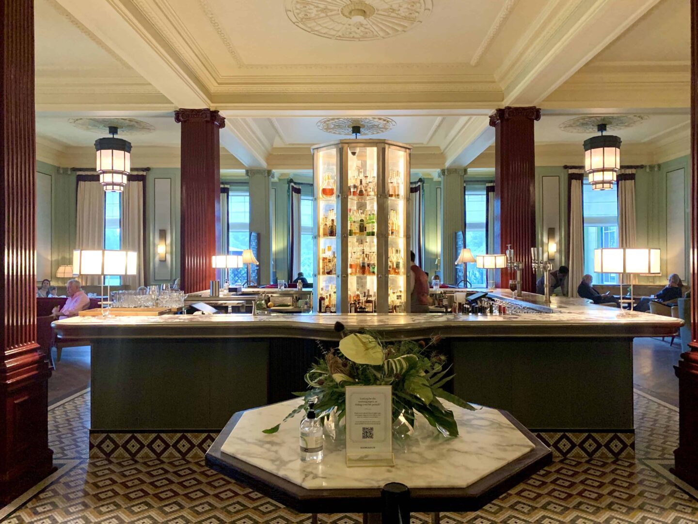 view inside the Century Bar at Gleneagles hotel with marble tops, red pillar posts and tiled floor centred around a lit up cabinet of alcohol