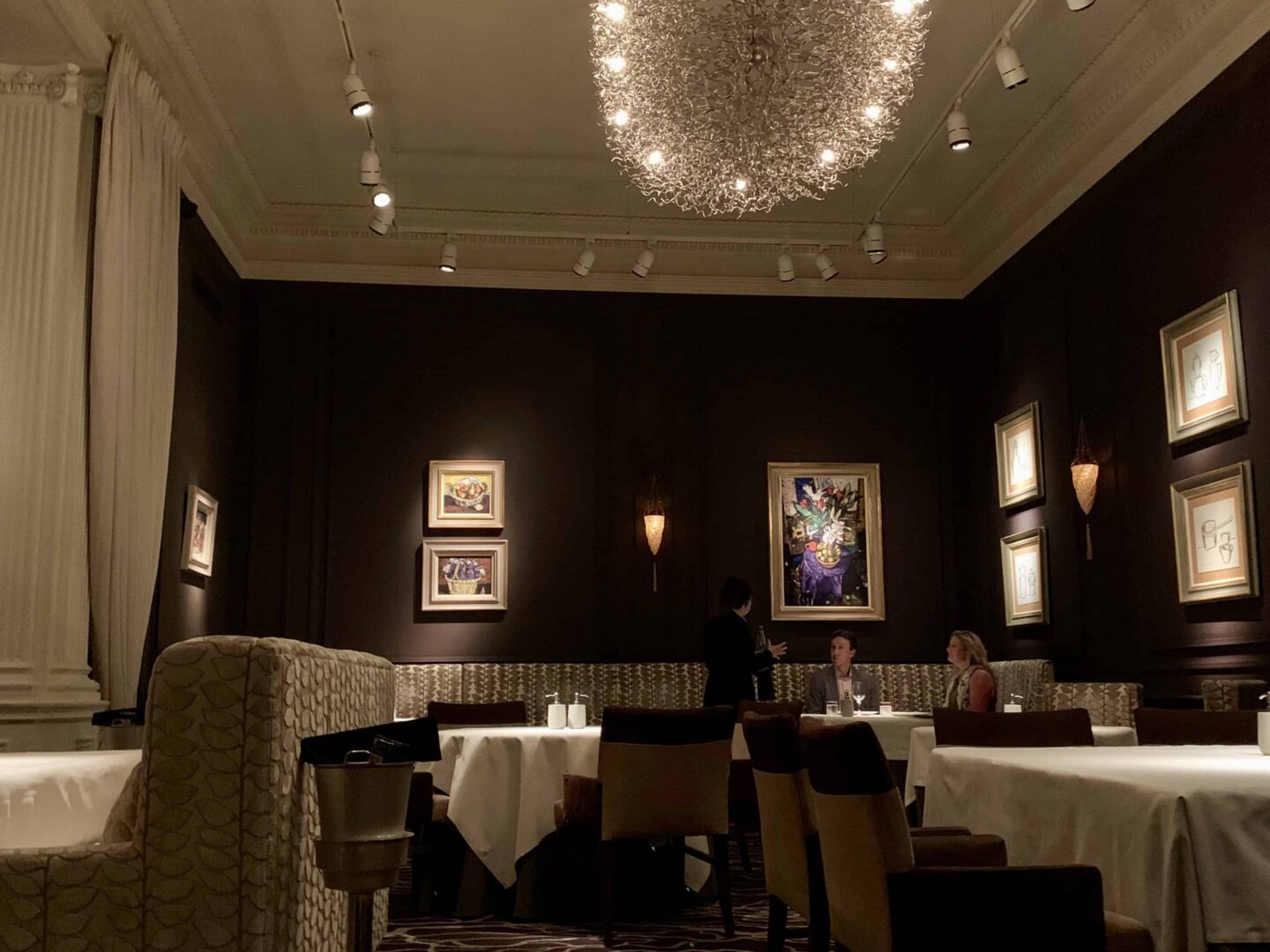 inside the Andrew Fairlie restaurant with dark surroundings, lights on paintings and silver centre ceiling display light