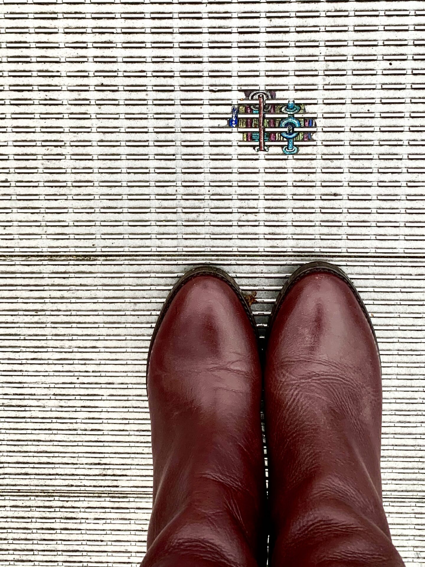 looking down towards brown leather shoes and the art work between metalworks of the bridge