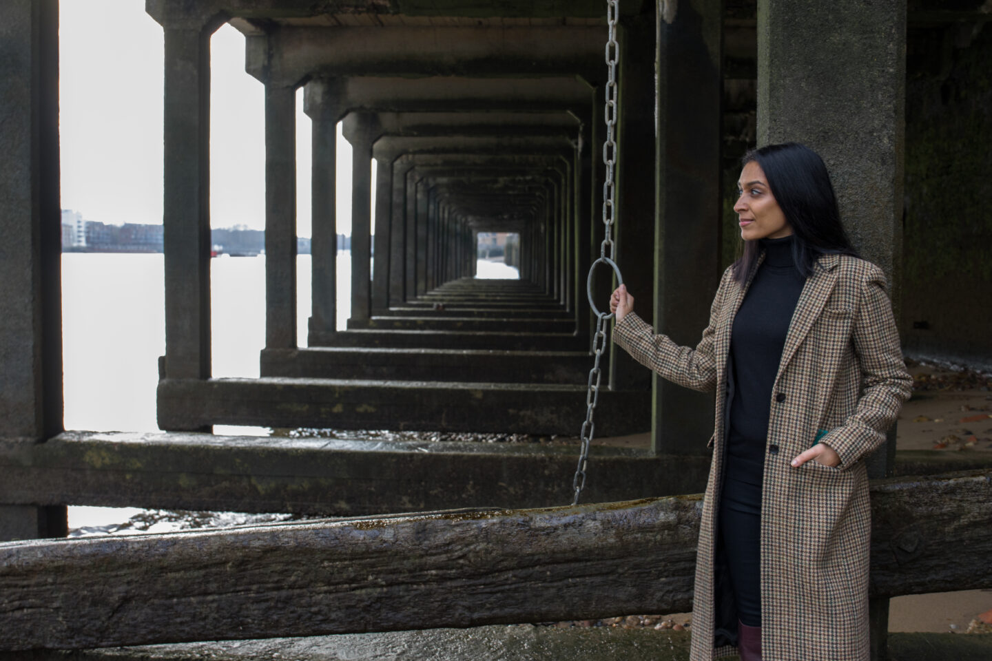 sima stood under the wooden pier holding a metal chain looking out towards the thames